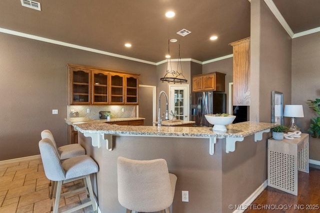 kitchen with stainless steel fridge with ice dispenser, glass insert cabinets, ornamental molding, baseboards, and a peninsula