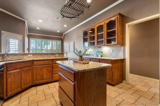 kitchen with a sink, ornamental molding, decorative backsplash, brown cabinets, and stone tile flooring