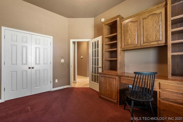 office area featuring built in desk, dark colored carpet, and baseboards
