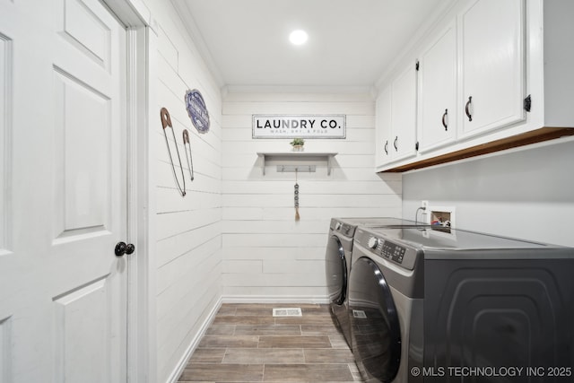 clothes washing area with cabinet space, washer and clothes dryer, wooden walls, and wood finished floors