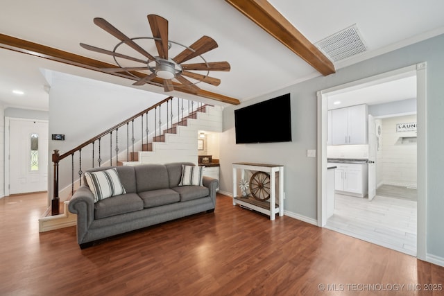 living room with stairs, wood finished floors, ceiling fan, baseboards, and beamed ceiling