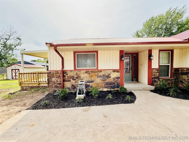 view of front of property with stone siding, a porch, a storage unit, an outdoor structure, and metal roof
