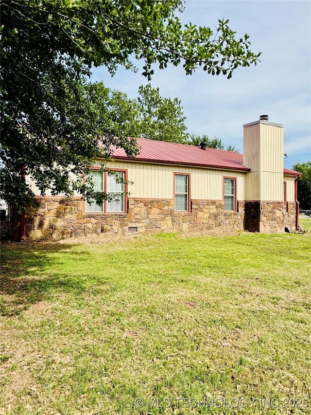 single story home featuring stone siding, a chimney, a front lawn, and metal roof