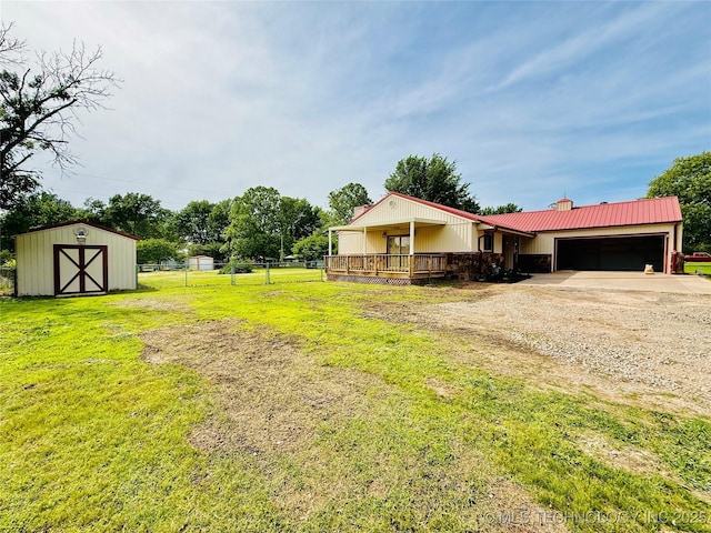 view of yard with driveway, an attached garage, an outdoor structure, a shed, and a deck