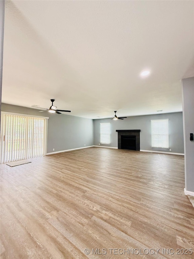 unfurnished living room featuring a ceiling fan, a fireplace, baseboards, and healthy amount of natural light