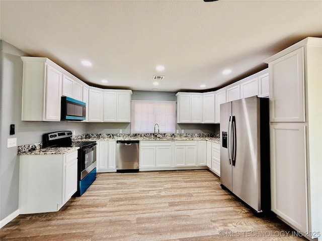 kitchen with appliances with stainless steel finishes, a sink, light wood-type flooring, white cabinetry, and light stone counters