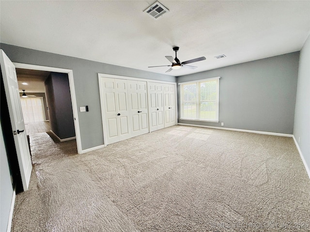 unfurnished bedroom with carpet, baseboards, ceiling fan, and two closets