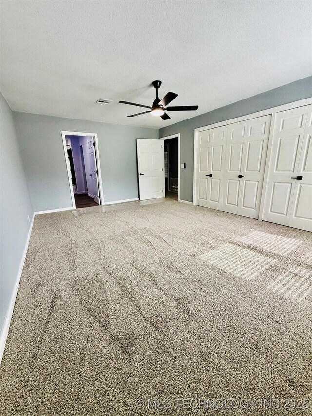 unfurnished bedroom with baseboards, carpet, multiple closets, a textured ceiling, and a ceiling fan