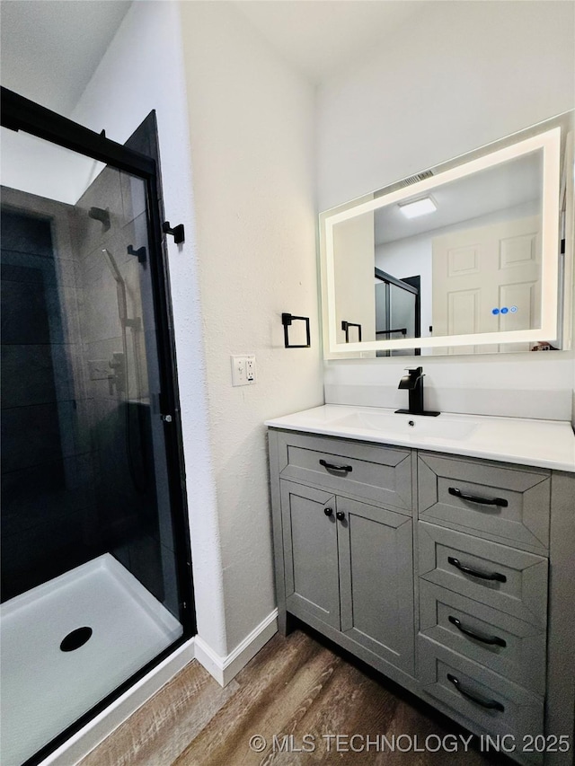 full bath with wood finished floors, a stall shower, baseboards, and vanity