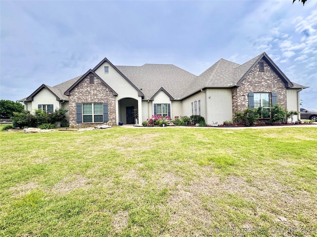 view of front of property featuring brick siding, a front yard, and roof with shingles