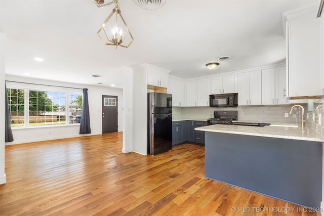 kitchen with black appliances, a peninsula, decorative backsplash, a sink, and light wood finished floors