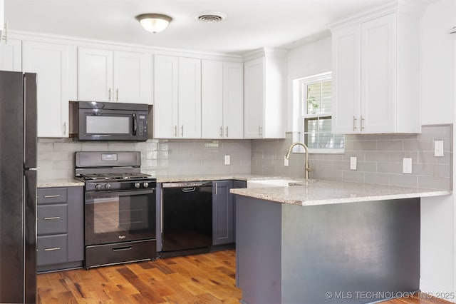 kitchen with black appliances, a sink, white cabinetry, light wood-style flooring, and backsplash