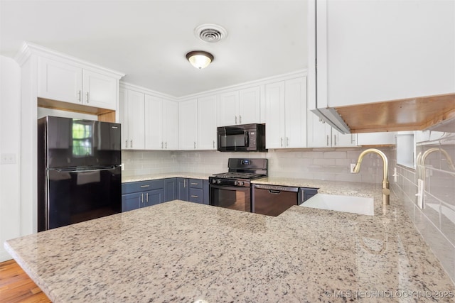 kitchen featuring black appliances, a sink, white cabinetry, light stone counters, and tasteful backsplash