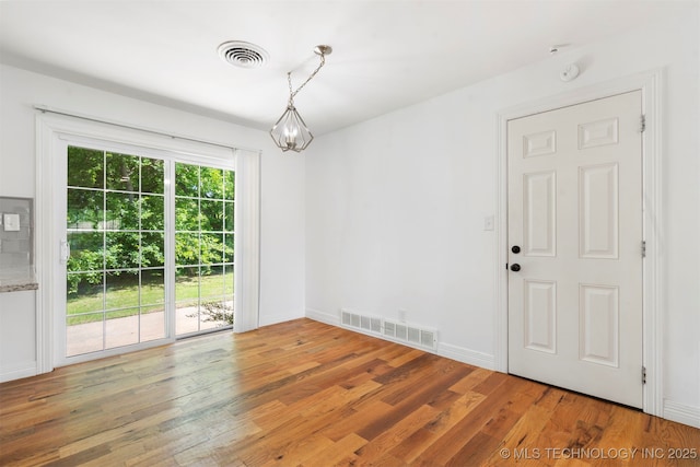 unfurnished dining area featuring wood finished floors, a chandelier, and baseboards