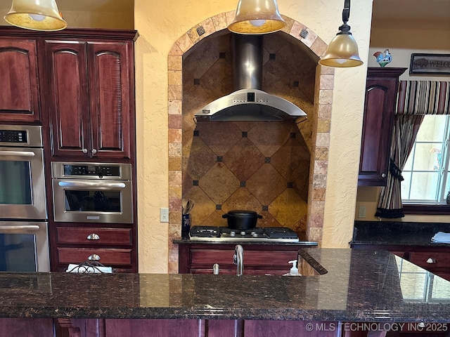 1216 N Oak Grove Rd, Drumright, OK 74030 - kitchen with stainless steel double oven, a textured wall, reddish brown cabinets, wall chimney range hood, and dark stone counters