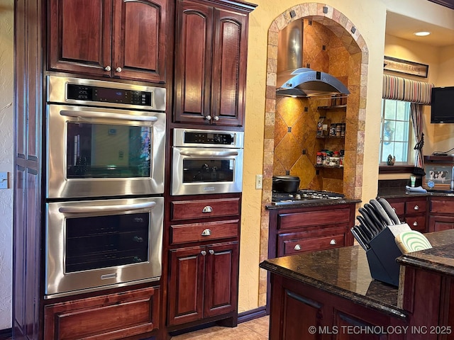 1216 N Oak Grove Rd, Drumright, OK 74030 - kitchen featuring appliances with stainless steel finishes, reddish brown cabinets, dark stone countertops, island exhaust hood, and a textured wall