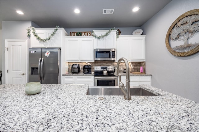 71 Rebel Ln, Durant, OK 74701 - kitchen with stainless steel appliances, a sink, white cabinets, decorative backsplash, and light stone counters