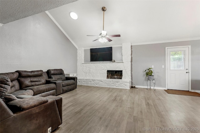 living room with a ceiling fan, vaulted ceiling, wood finished floors, a stone fireplace, and ornamental molding