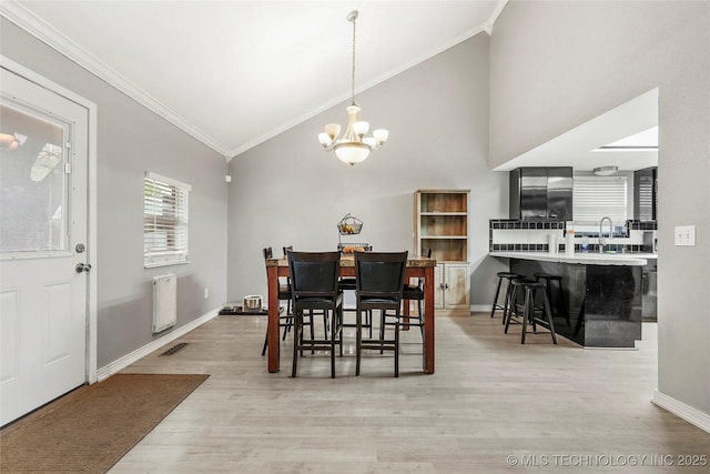 dining area with crown molding, vaulted ceiling, a chandelier, light wood-type flooring, and baseboards
