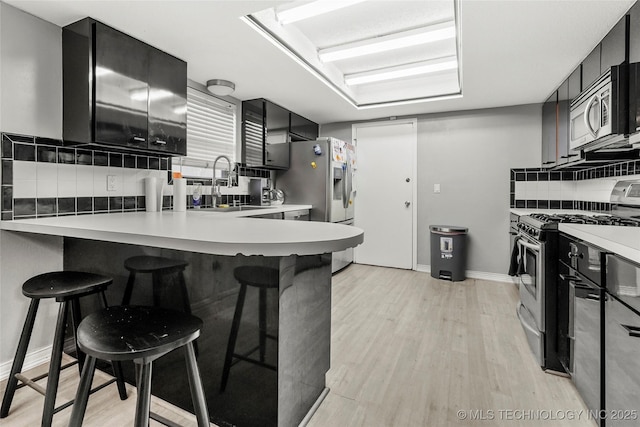 kitchen featuring appliances with stainless steel finishes, a kitchen bar, decorative backsplash, light wood-style flooring, and light countertops