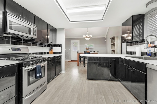 kitchen with stainless steel appliances, a chandelier, dark cabinetry, and crown molding