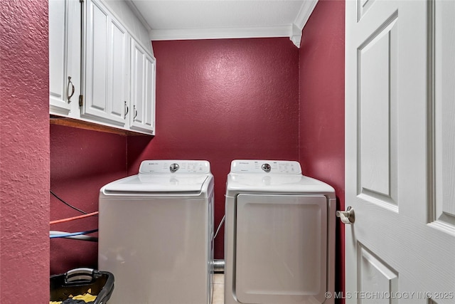clothes washing area featuring washing machine and clothes dryer, a textured wall, cabinet space, and ornamental molding