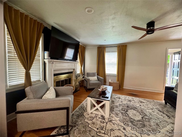 2009 S Osage Ave, Bartlesville, OK 74006 - living room featuring a glass covered fireplace, baseboards, wood finished floors, ceiling fan, and a textured ceiling