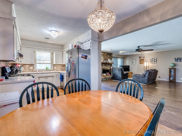 124 Canterbury Ct, Bartlesville, OK 74006 - dining area with a textured ceiling, light wood-type flooring, ceiling fan, a fireplace, and a chandelier