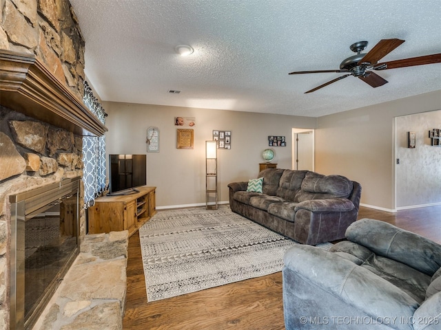 124 Canterbury Ct, Bartlesville, OK 74006 - living room featuring a textured ceiling, a ceiling fan, baseboards, a stone fireplace, and wood finished floors