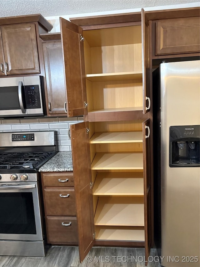 823 Sooner Park Dr, Bartlesville, OK 74006 - kitchen featuring appliances with stainless steel finishes, wood finished floors, stone counters, and open shelves
