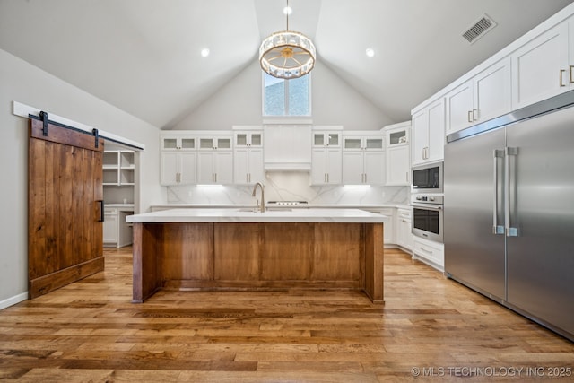 682 W 113th Ct S, Jenks, OK 74037 - kitchen with built in appliances, light countertops, light wood-type flooring, a barn door, and a center island with sink