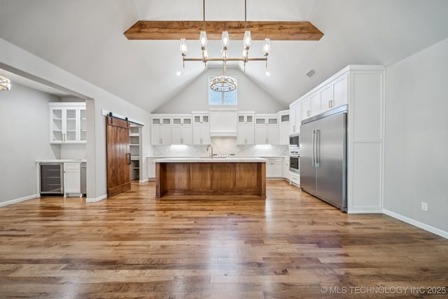 682 W 113th Ct S, Jenks, OK 74037 - kitchen with built in appliances, wine cooler, a barn door, wood finished floors, and beamed ceiling