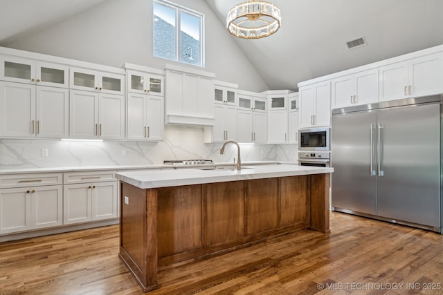 682 W 113th Ct S, Jenks, OK 74037 - kitchen featuring built in appliances, tasteful backsplash, high vaulted ceiling, white cabinets, and wood finished floors