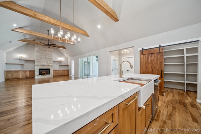 682 W 113th Ct S, Jenks, OK 74037 - kitchen featuring ceiling fan, beamed ceiling, a fireplace, brown cabinetry, and a barn door
