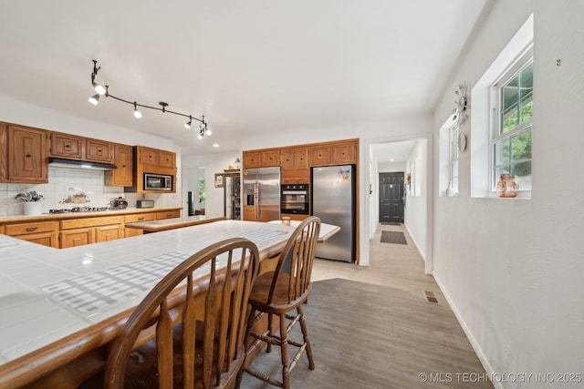 239 Seneca Dr, Sand Springs, OK 74063 - kitchen with stainless steel appliances, tile counters, decorative backsplash, light wood-type flooring, and under cabinet range hood