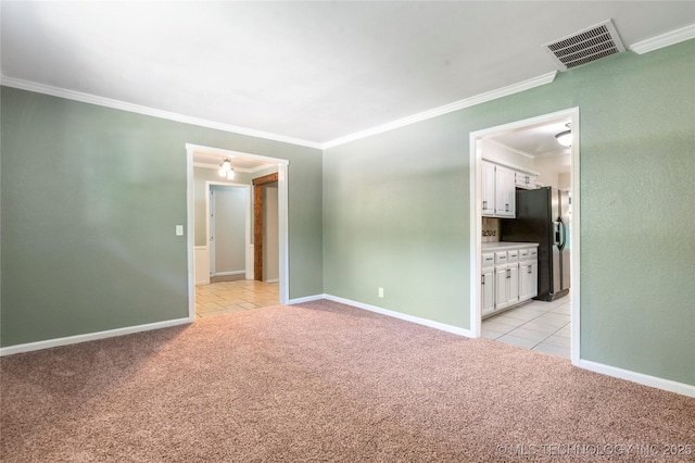 empty room featuring light carpet, crown molding, light tile patterned flooring, and baseboards