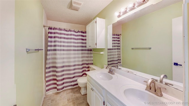 full bath with a textured ceiling, toilet, double vanity, and curtained shower
