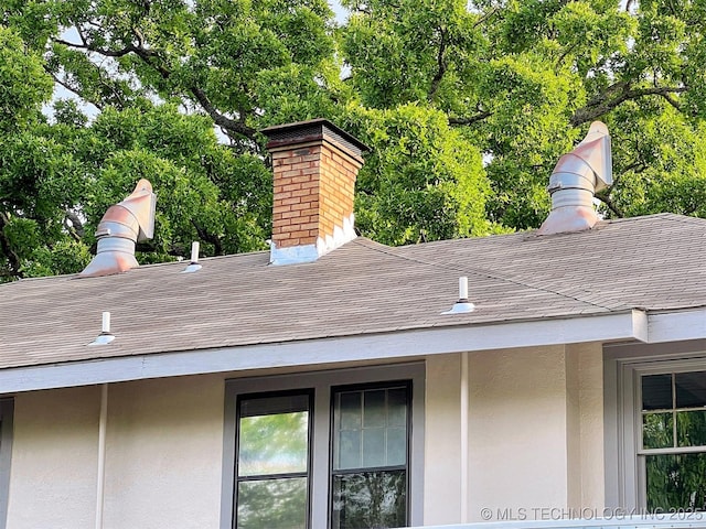 525 W Downing St, Tahlequah, OK 74464 - exterior view of roof with shingles, stucco siding, a chimney, and view of scattered trees