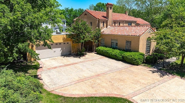 mediterranean / spanish-style house featuring a tile roof, concrete driveway, fence, a chimney, and brick siding