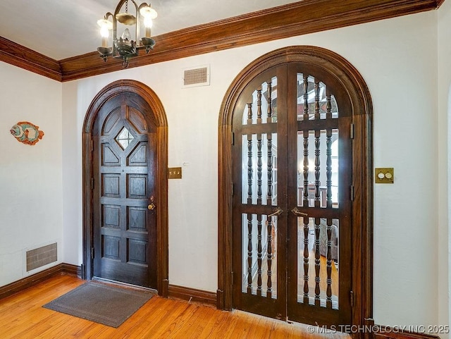foyer entrance with arched walkways, ornamental molding, wood finished floors, baseboards, and a chandelier