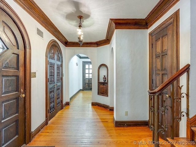 foyer featuring arched walkways, ornamental molding, light wood-type flooring, and baseboards