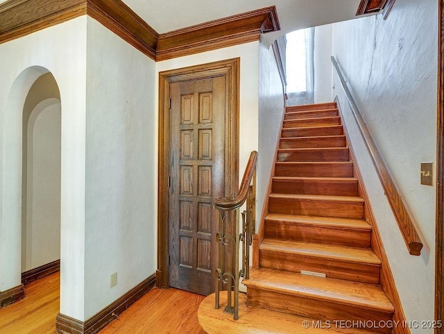 stairway featuring wood finished floors, crown molding, arched walkways, and baseboards