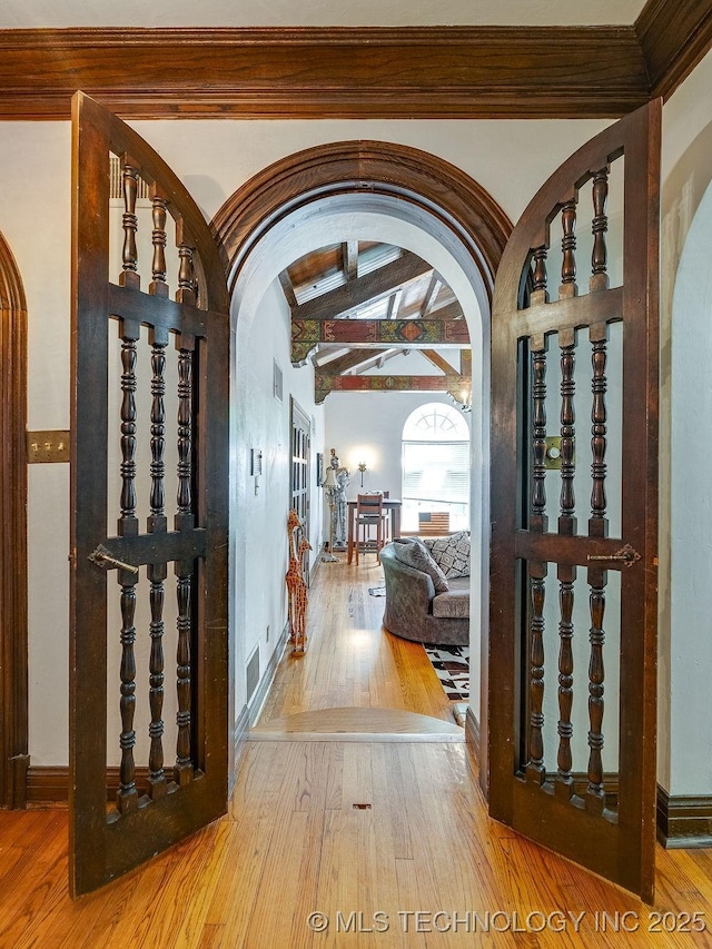 foyer featuring arched walkways, hardwood / wood-style flooring, beamed ceiling, and baseboards