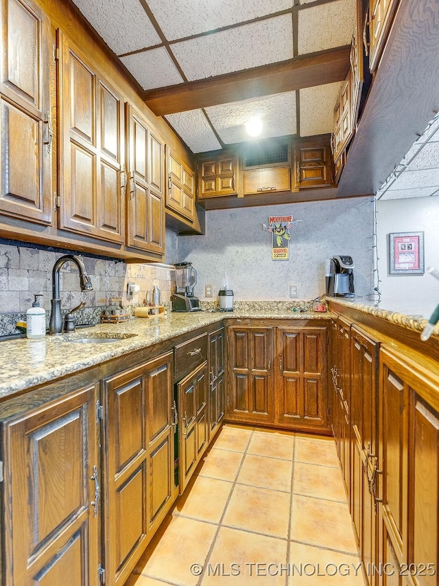 kitchen with a sink, light tile patterned floors, decorative backsplash, light stone countertops, and brown cabinets