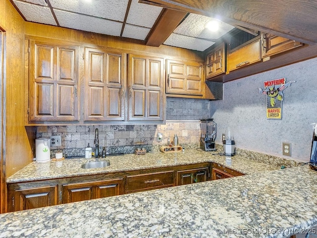 kitchen with tasteful backsplash, brown cabinetry, light stone counters, and a sink