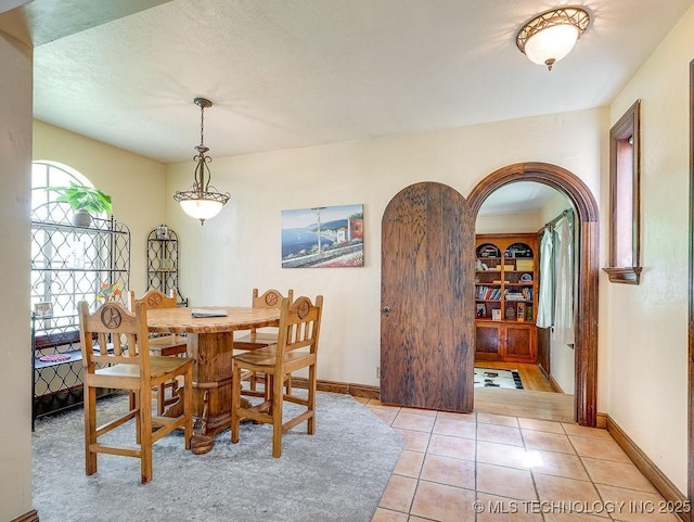 dining space with arched walkways, light tile patterned floors, and baseboards