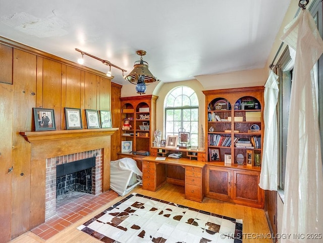 office area with light wood-style floors, a brick fireplace, and rail lighting