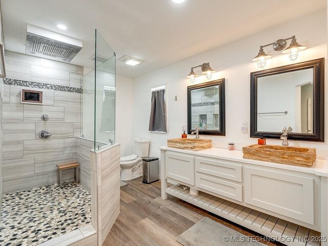 full bathroom with a tile shower, wood finished floors, toilet, double vanity, and recessed lighting