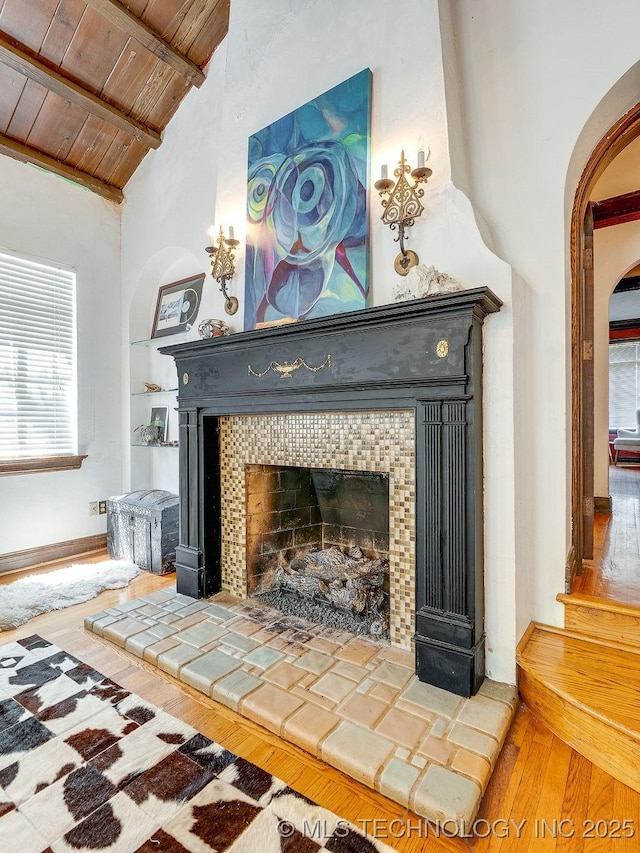 detailed view of a tile fireplace, wood ceiling, wood finished floors, arched walkways, and beam ceiling