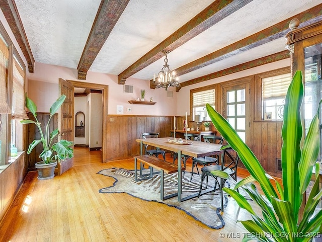 dining room with wooden walls, wood-type flooring, a wainscoted wall, beam ceiling, and a chandelier